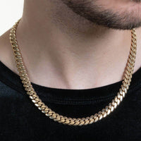 A close-up of a person wearing the Cuban Link Chain - Ready to Ship Solid Gold over a black shirt, highlighting the lower face, neck, and jawline with trimmed facial hair.