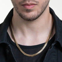 Close-up of a man wearing the Cuban Link Chain - Ready to Ship Solid Gold with a black T-shirt and jacket. Only his lower face, neck, and chest are shown.