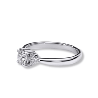 The Round Brilliant Cut Diamond Engagement Ring features a central round diamond with smaller side diamonds, shown against a plain white background.