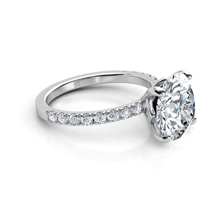 The Round Cut Lab Diamond Engagement Ring with Pave Band showcases a large round lab diamond in a four-prong white gold setting, accented by pavé-set diamonds along the band for added sparkle.