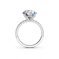The Round Cut Lab Diamond Engagement Ring with Pave Band showcases a large round lab diamond in a prong setting, accented by pavé-set diamonds along the band, all displayed against a white background.