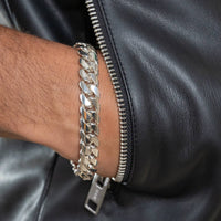 A close-up of a wrist wearing the Silver Cuban Link Bracelet - 12mm, partially hidden beneath the sleeve of a black leather jacket with a visible zipper.