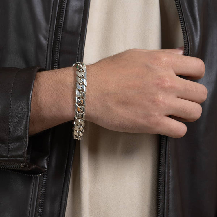 A person wearing the 12mm Handmade Miami Cuban Link Bracelet - 950 Silver and a dark leather jacket over a light shirt, with their hand resting near the jacket zipper.