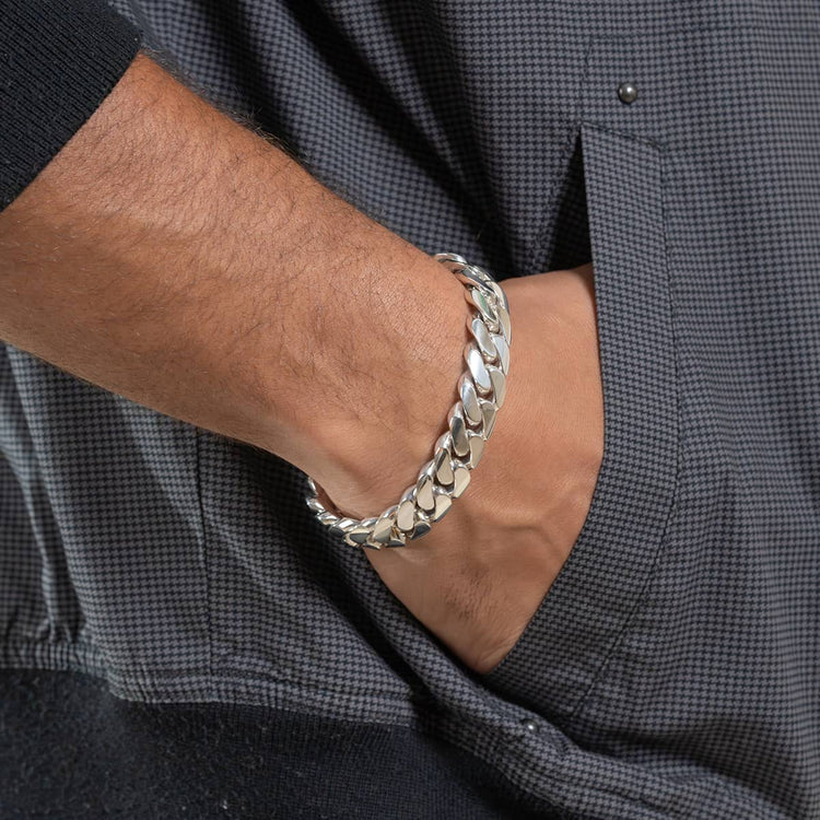 A close-up of a hand wearing the 14mm Handmade Miami Cuban Link Bracelet - 950 Silver, with the bracelet partially tucked into the pocket of dark, textured clothing.