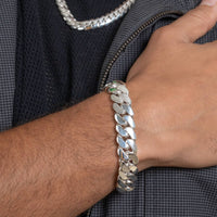 A close-up of a wrist wearing the Silver Cuban Link Bracelet - 14mm. The person holds their gray textured jacket, and a matching silver chain necklace is partially visible.