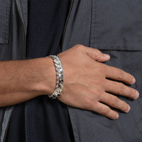 Wearing the Silver Cuban Link Bracelet - 14mm on their wrist, a person rests their hand on their chest while dressed in a dark, textured jacket with a visible zipper.