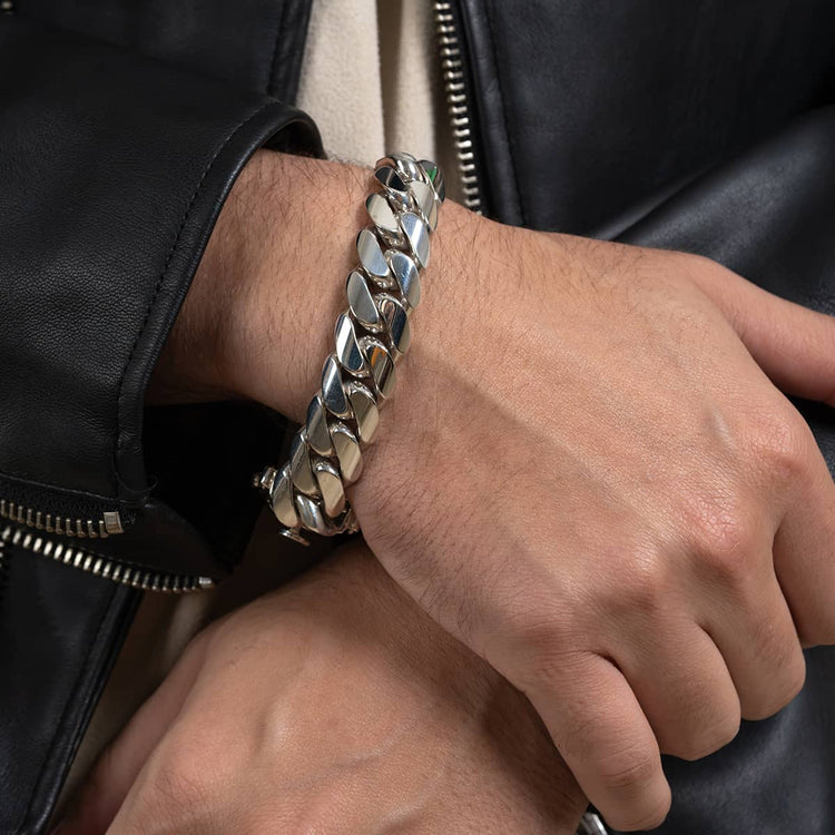 A person wearing a 16mm Handmade Miami Cuban Link Bracelet - 950 Silver on their wrist, paired with a black leather jacket with a visible zipper and a light-colored shirt underneath.