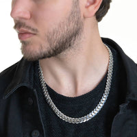 A man with a short beard and mustache, dressed in a black shirt and jacket, is shown in close-up wearing the Silver Cuban Link Chain - 10mm around his neck as he looks slightly to the side.