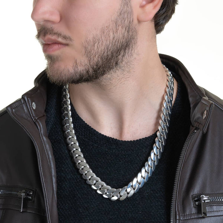 A man with a short beard wears a black sweater, brown leather jacket, and the 16mm Handmade Miami Cuban Link Chain - 950 Silver. The photo is cropped at his nose, highlighting the striking silver necklace on his neck and chest.