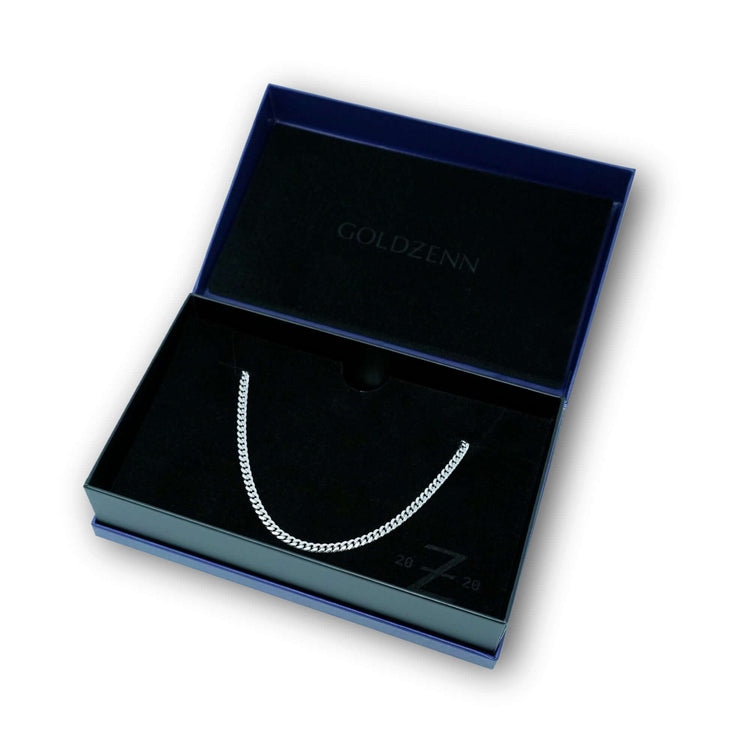 The Silver Cuban Link Chain - 5mm in 925 Sterling Silver is shown in an open dark jewelry box with GOLDZENN on the lid and a plush black velvet interior.