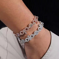 A close-up of a wrist with two sparkling chain-link bracelets—one rose gold and the Silver Moissanite Cross Infinity Bracelet, both embellished with diamonds and featuring star and cross charms. The wearer has on a black sleeve.