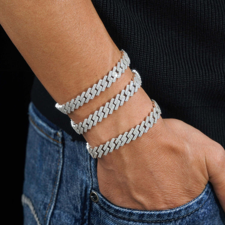 A person in a black top and blue jeans wears three 925 silver zigzag bracelets stacked on their wrist, including the Silver Moissanite Cuban Link Bracelet – 10mm, with their hand resting casually in their pocket.