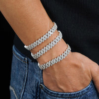 A person in a black top and blue jeans wears three 925 silver zigzag bracelets stacked on their wrist, including the Silver Moissanite Cuban Link Bracelet – 10mm, with their hand resting casually in their pocket.