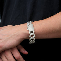 Wearing the Silver Moissanite Cuban Link Bracelet – 20mm, encrusted with sparkling stones, a person rests their hand on their wrist against a plain black shirt.