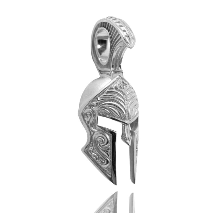 The Silver Spartan Helmet Pendant is crafted in the shape of an ancient Greek helmet with detailed engravings and a top loop for a chain, elegantly displayed on a reflective surface.