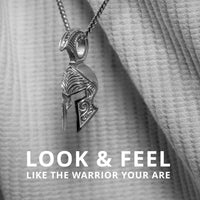 The Silver Spartan Helmet Pendant hangs on a chain against textured fabric. The text says: LOOK & FEEL LIKE THE WARRIOR YOU ARE.