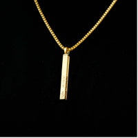 The Solid Name Bar Pendant features a vertical gold bar with personalized engraved text, creating a stylish piece of jewelry that stands out elegantly against a black background.