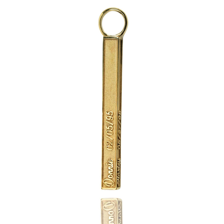 The Solid Name Bar Pendant is a gold necklace featuring a bar pendant with a round top loop, engraved with "Donie" and "02/05/95." This personalized jewelry piece is elegantly displayed on a reflective white surface.