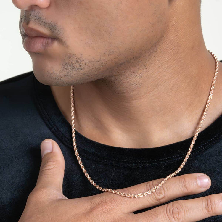 A person wears a black shirt and a Rope Chain - 2mm-5mm Solid Rose Gold necklace, with one hand resting on their chest. The photo highlights the lower face, neck, and the rose gold rope chain.