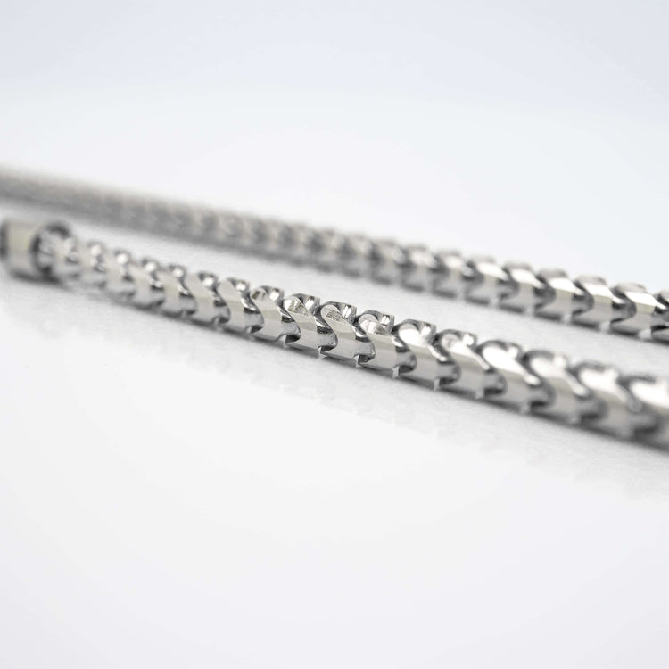 Close-up of two metallic, spiral-shaped rods parallel on a white surface, capturing the intricate design of the Franco Chain - 1.8mm-6.5mm Solid White Gold, set against a softly blurred background.