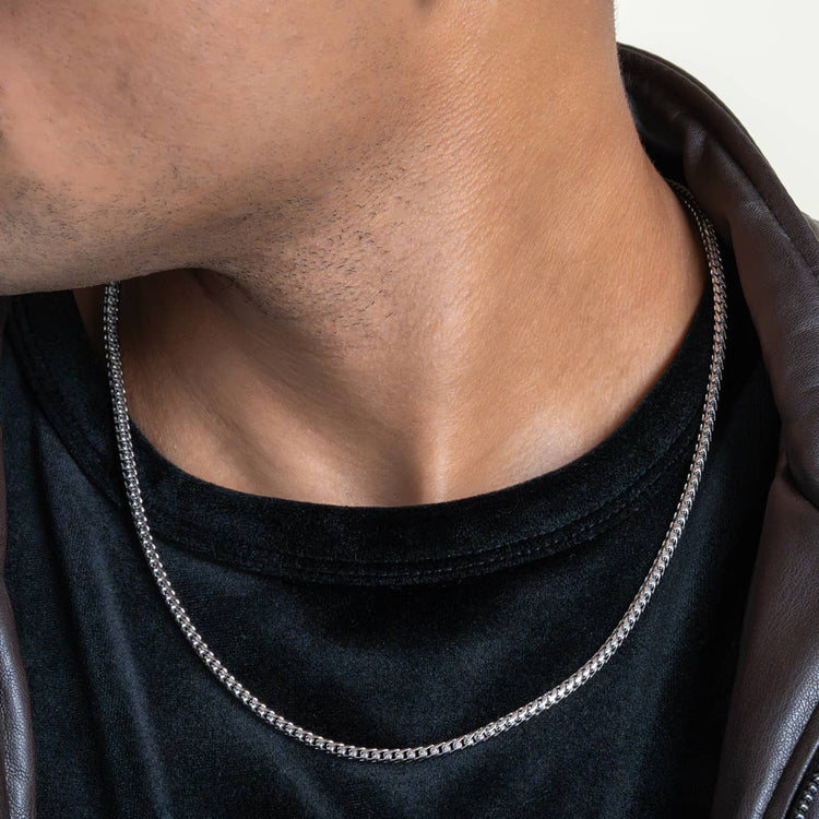 Close-up of a person wearing the Franco Chain - 1.8mm-6.5mm Solid White Gold over a black shirt and dark jacket. The face is partially out of frame, emphasizing the neck and this elegant white gold jewelry.