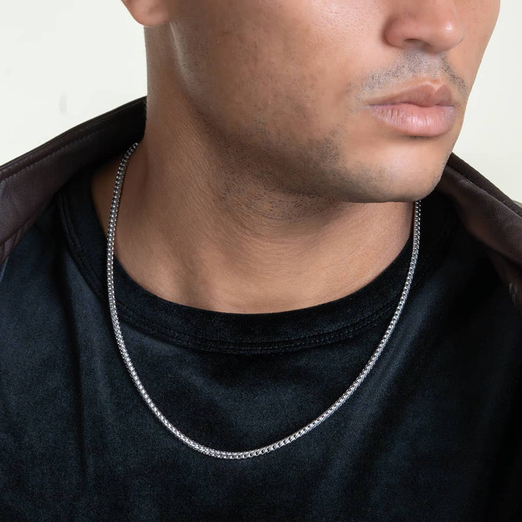 Someone wears a Franco Chain - 1.8mm-6.5mm Solid White Gold necklace over a black shirt, with a brown jacket draped over their shoulders. Only their lower face, neck, and upper chest are visible.