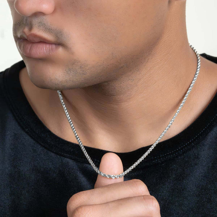 A man in a black shirt holds the Rope Chain - 2mm-5mm Solid White Gold between his fingers, highlighting its intricate details; only the lower half of his face and neck are shown.