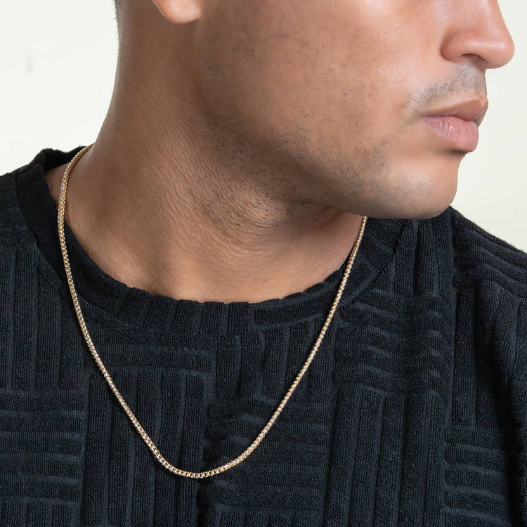 A person wearing a textured black shirt and the Franco Chain Two Tone Prism Cut - 3mm 10k Solid Gold necklace, shown from the shoulders up, facing slightly to the side against a plain, neutral background.