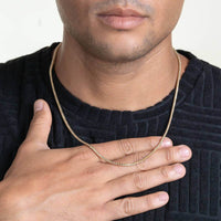 A person in a black textured shirt rests their hand on their chest, showcasing the Franco Chain Two Tone Prism Cut - 2.5mm 14k Solid Gold. The image captures the lower face, neck, hand, and upper chest.