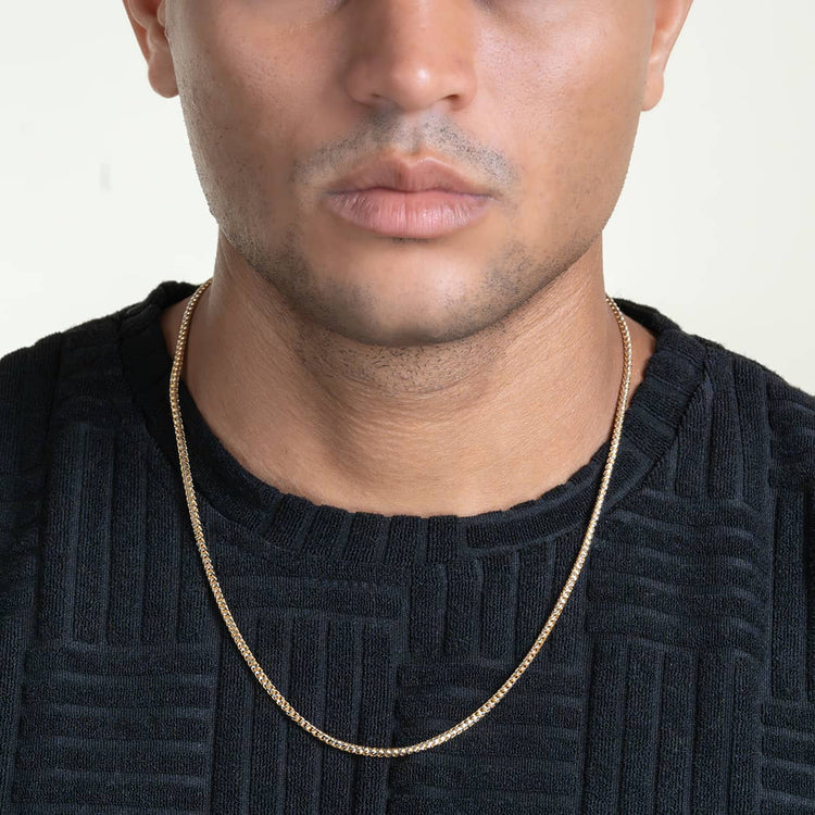 A person wearing a textured black shirt and the Franco Chain Two Tone Prism Cut - 3mm 10k Solid Gold necklace, shown from shoulders to mouth against a plain light background.