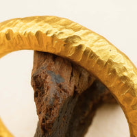 Close-up of the 24k - 4mm Hammered Donut Ring, featuring a textured finish and resting on rough brown stone against a light background.