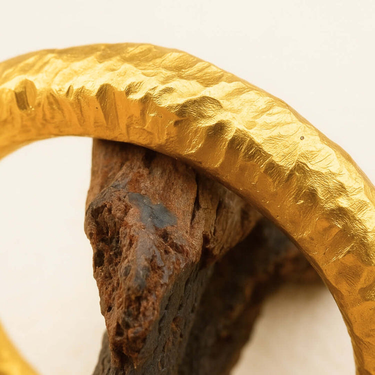Close-up of the 24k - 4mm Hammered Donut Ring, featuring a textured finish and resting on rough brown stone against a light background.