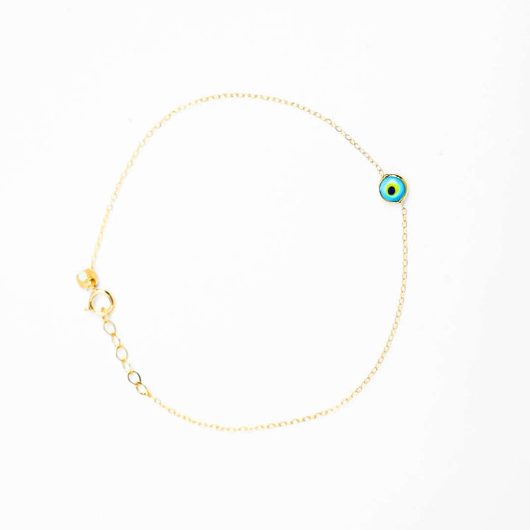 The one lucky eye bracelet - 14k features a delicate 14k gold chain with a blue, white, and black enamel evil eye charm for spiritual protection. It has an adjustable clasp and is shown on a white background.