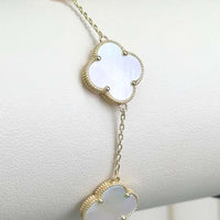 The 5 Leaf Clover Bracelet in 14k yellow gold showcases white mother-of-pearl charms and is elegantly displayed on a lightly textured surface.
