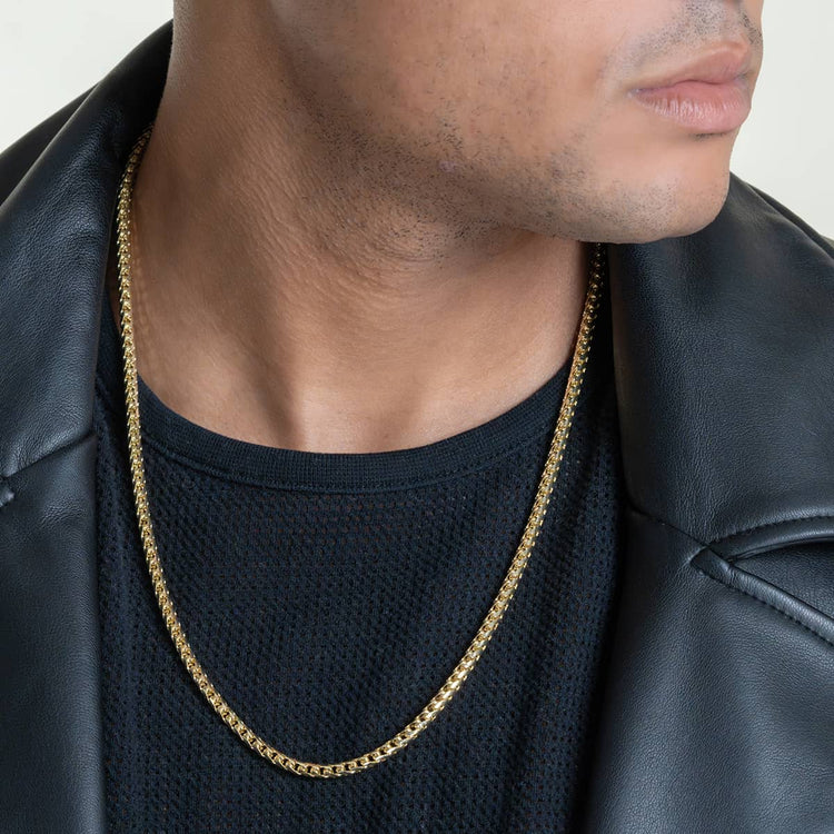 A person in a black shirt and leather jacket is shown from the chin down, showcasing the Franco Chain- 1.8mm-6.5mm Solid Yellow Gold necklace around their neck.