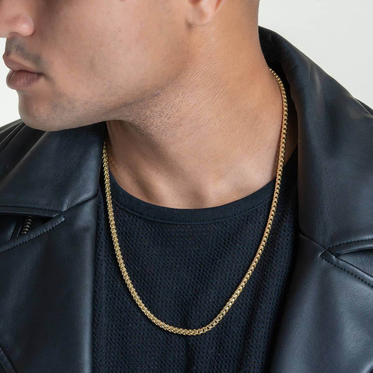 A person is shown from the shoulders up, their face partially visible, wearing a black textured shirt, black leather jacket, and the Franco Chain-1.8mm-6.5mm Solid Yellow Gold necklace.