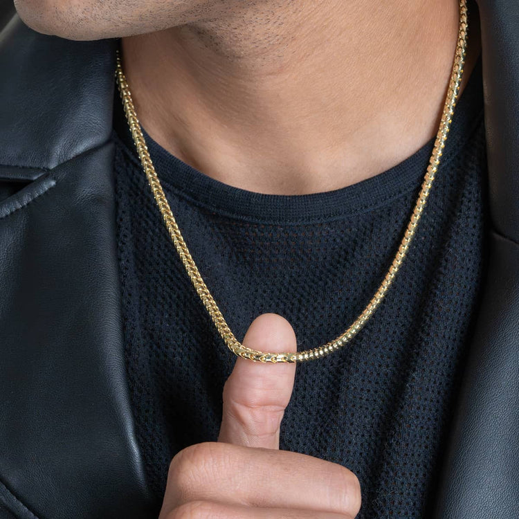A person wearing a black mesh shirt and leather jacket holds the Franco Chain- 1.8mm-6.5mm Solid Yellow Gold with their thumb and finger, showcasing this striking yellow gold jewelry around their neck.