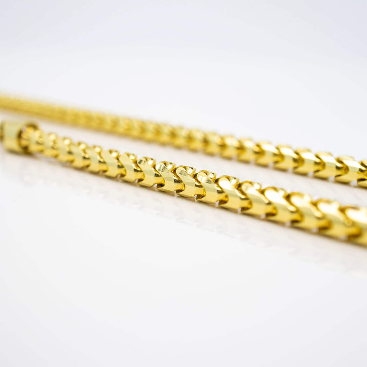 Close-up of two Franco Chain necklaces (1.8mm-6.5mm) in solid yellow gold with a polished, shiny finish, laying parallel on a white reflective surface. The chains feature a classic curb link design.
