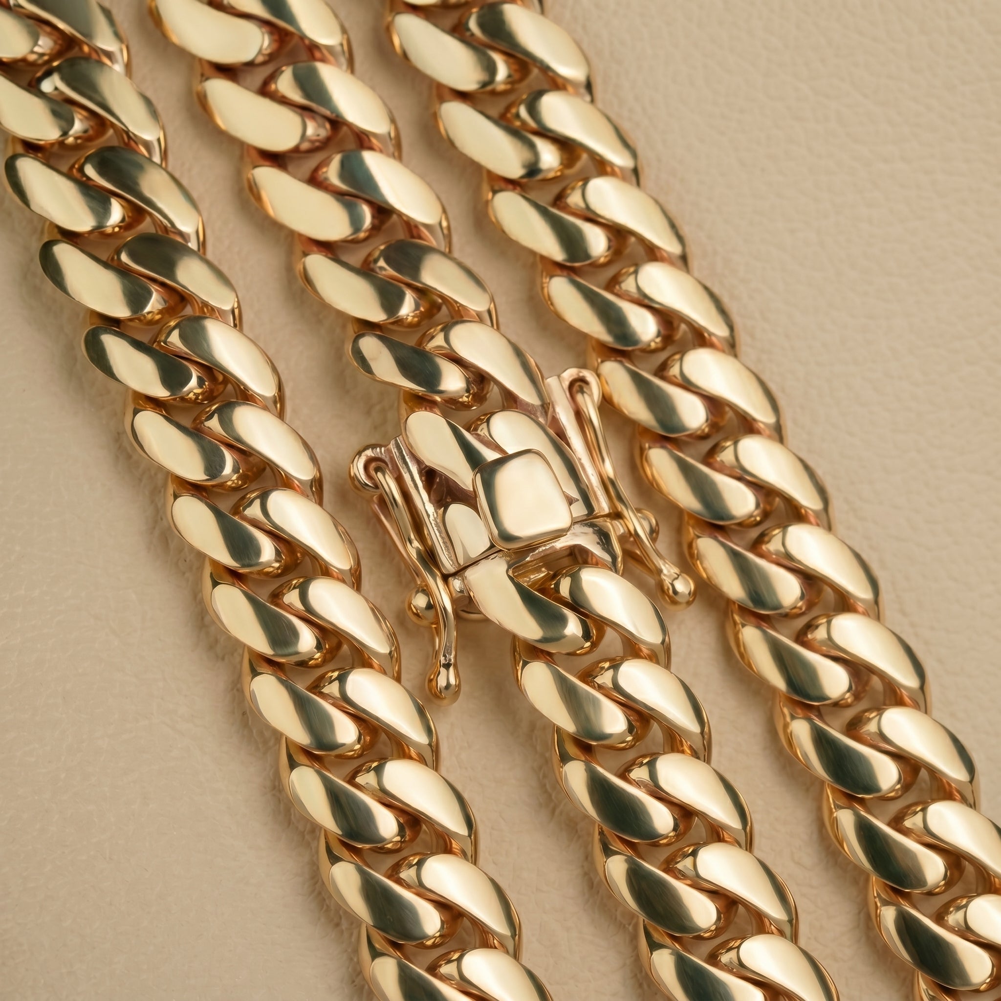 Close-up of three 6mm Handmade Miami Cuban Link Chains in 10K solid gold with box clasps, shown on a beige textured surface. Ready to ship.