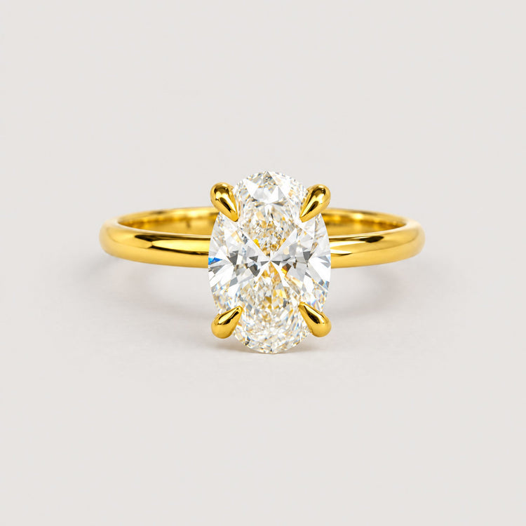 The 1.72ct oval-cut lab diamond engagement ring, set in 14k solid yellow gold, features a solitaire stone held by four prongs and is displayed on a warm off-white studio background.