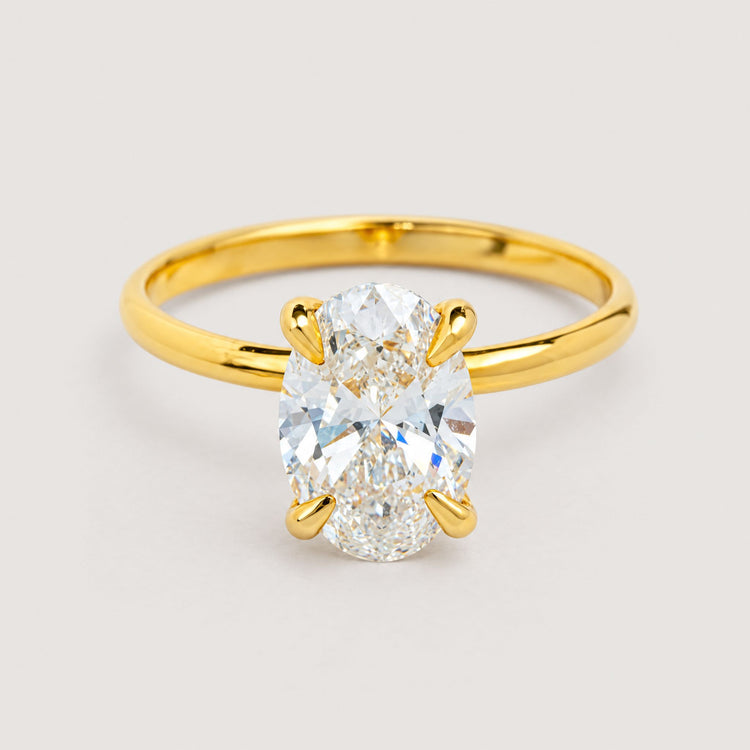 A 1.72ct oval-cut lab diamond engagement ring in 14k solid yellow gold is showcased elegantly against a warm off-white studio background.
