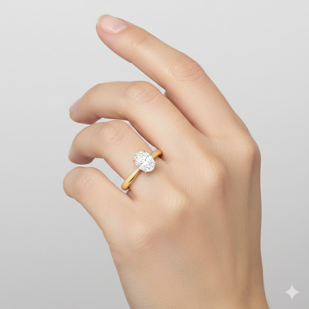 A hand with neatly manicured nails wears the 1/4 CT Diamond Oval Solitaire Ring in 14K Gold, showcasing its sparkling oval diamond against a simple light background.