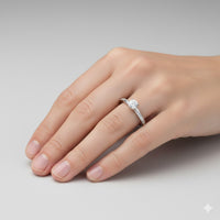 A hand with neatly manicured nails wears the Brilliance Eternity Lab Grown Diamond Engagement Ring, showcasing a round center stone and smaller diamonds along the band against a plain light gray background.