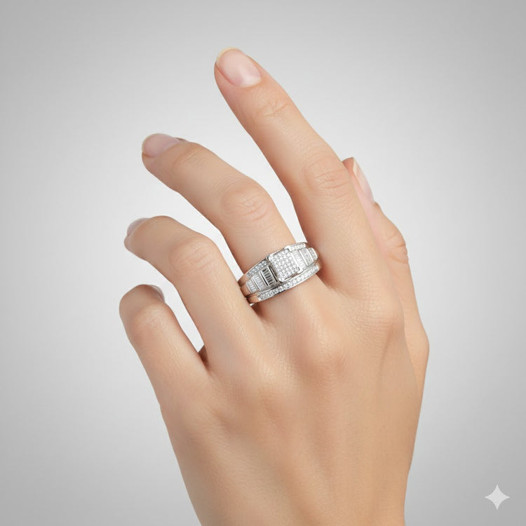 A hand with manicured nails wears the Sterling Silver Diamond Cluster Bridal Engagement Ring, featuring rectangular stones and a round diamond cluster, showcased against a plain light gray background.