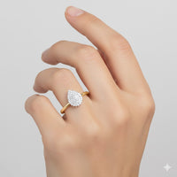 A hand with manicured nails showcases the 10k Yellow Gold 1/6CT Diamond Pear Gift Ring, featuring a pear-shaped cluster of sparkling diamonds, set against a simple light background.