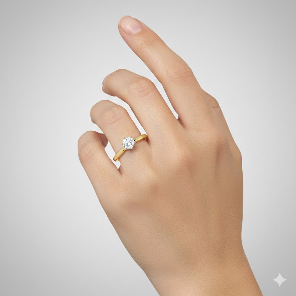 A hand wearing the 14k Yellow Gold Diamond Solitaire Bridal Ring 3/8 Cttw on the ring finger is displayed against a plain, light gray background.