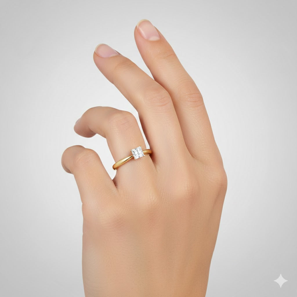 A light-skinned hand wears the 1/4CT Princess Diamond Solitaire Ring in 14K Gold, featuring a striking natural diamond on the ring finger against a plain light gray background.