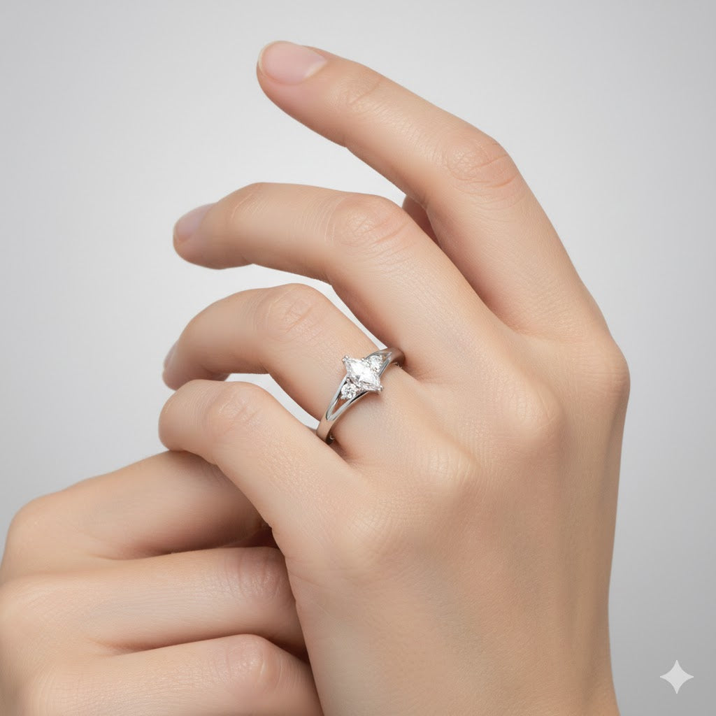 A hand with manicured nails wears the Marquise Lab Diamond Three-Stone Engagement Ring in Platinum Finish, featuring a large, clear marquise lab diamond on a simple band against a plain, light background.