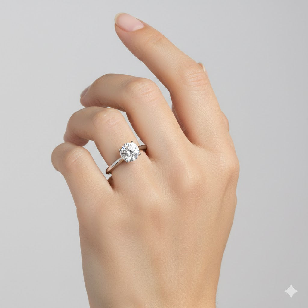 A hand with a light skin tone is shown against a neutral background, wearing the Classic Round Solitaire Lab Grown Diamond Engagement Ring featuring a large round lab-grown diamond on the ring finger.