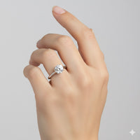 A hand with a light skin tone is shown against a neutral background, wearing the Classic Round Solitaire Lab Grown Diamond Engagement Ring featuring a large round lab-grown diamond on the ring finger.